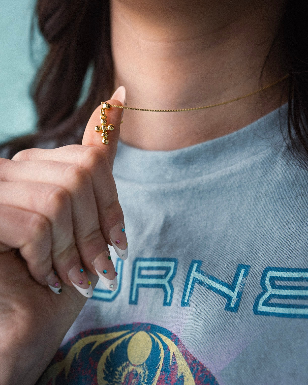 Person wearing a gold necklace with a cross pendant, holding it up to the camera.