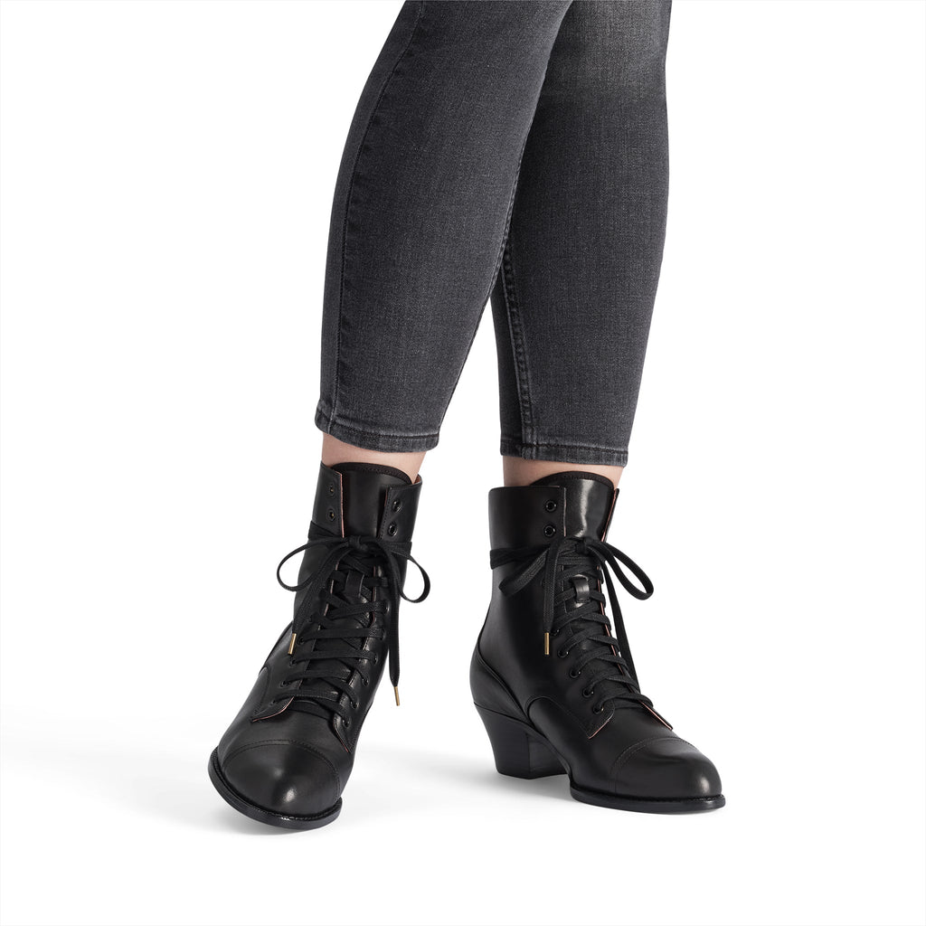 Black lace-up boots worn with gray jeans on a white background