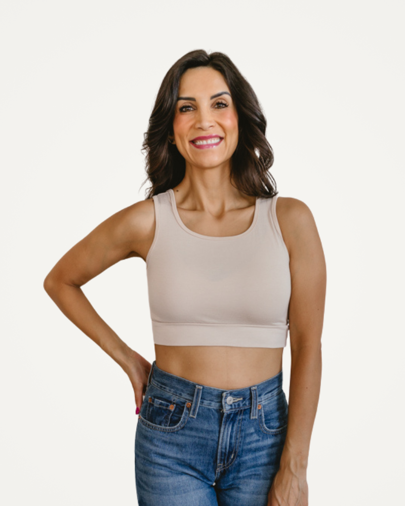Woman wearing a beige tank top and blue jeans on a white background