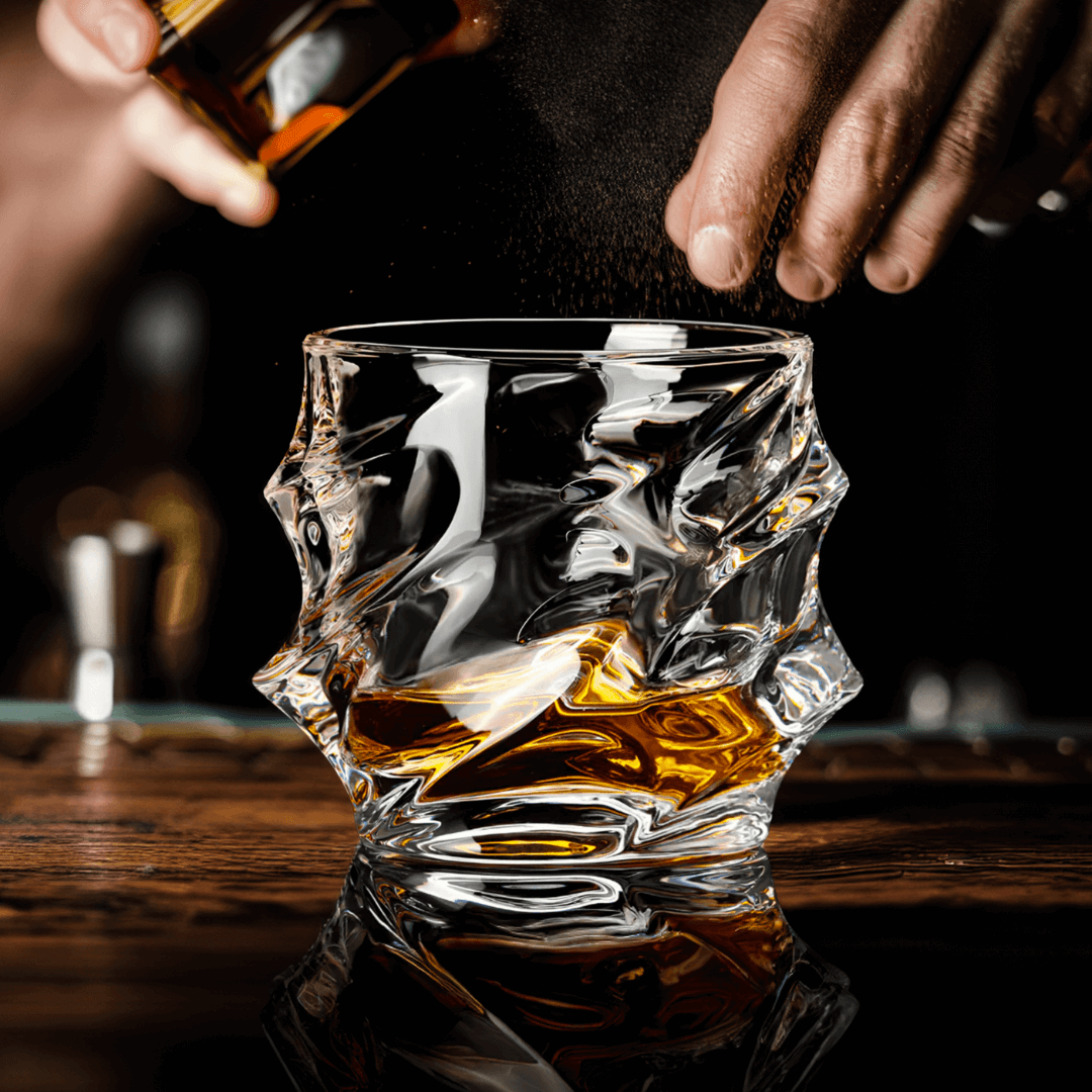 Person pouring whiskey into a textured glass on a wooden surface