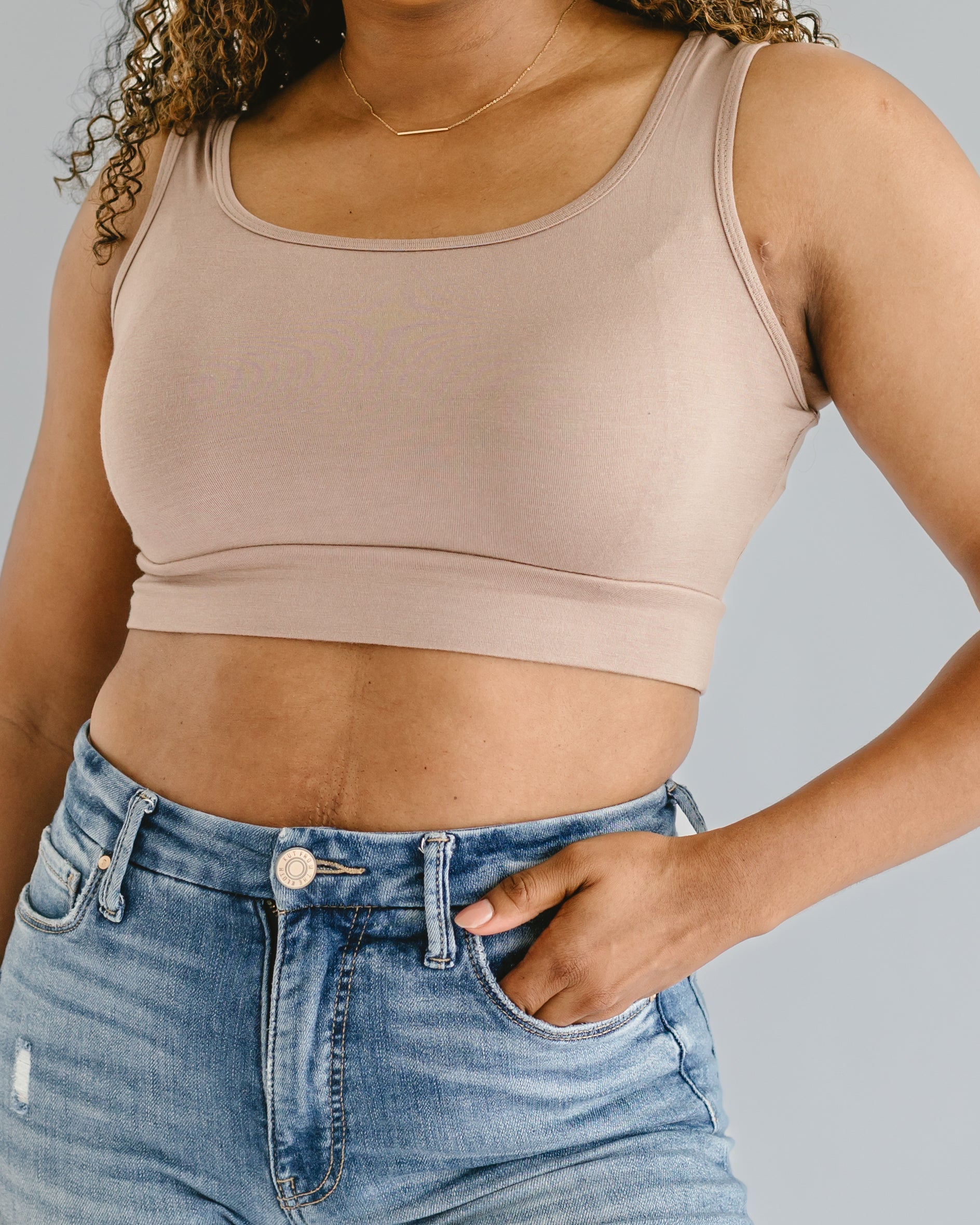 Person wearing a beige tank top and blue jeans on a gray background