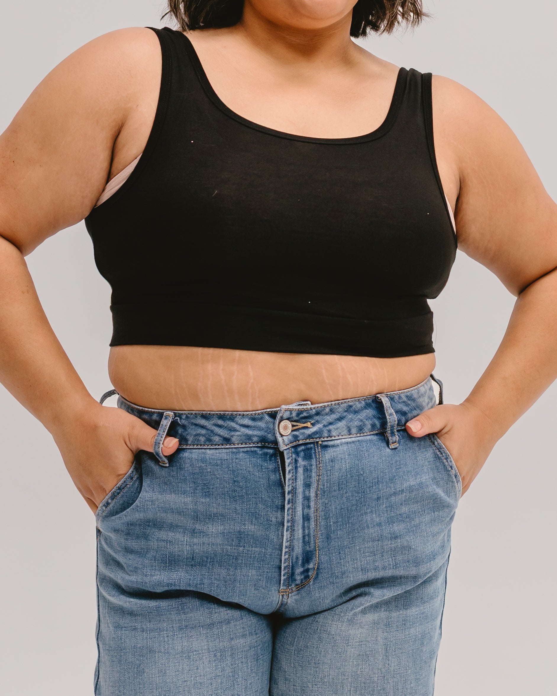 Person wearing a black tank top and blue jeans against a plain background