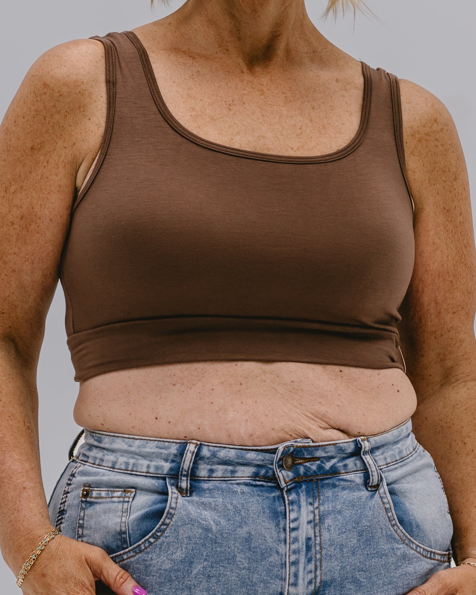 Person wearing a brown tank top and blue jeans against a neutral background