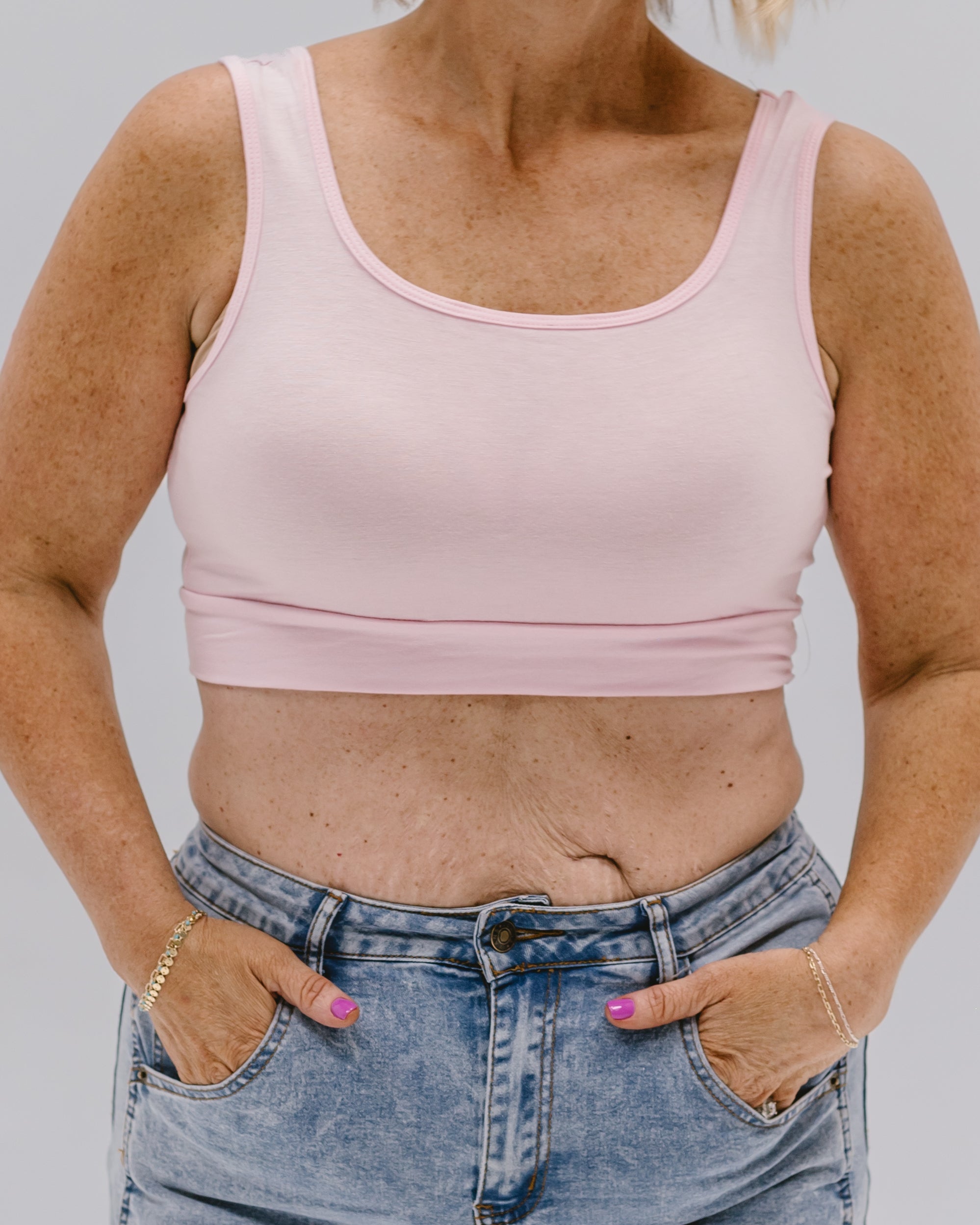 Person wearing a pink tank top and blue jeans against a plain background