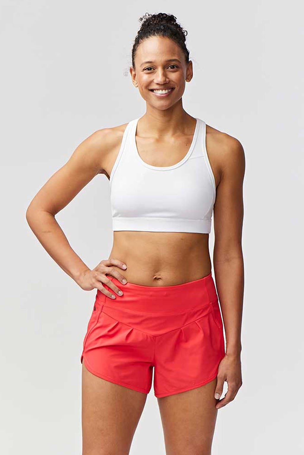 Woman wearing a white sports bra and red shorts on a light gray background