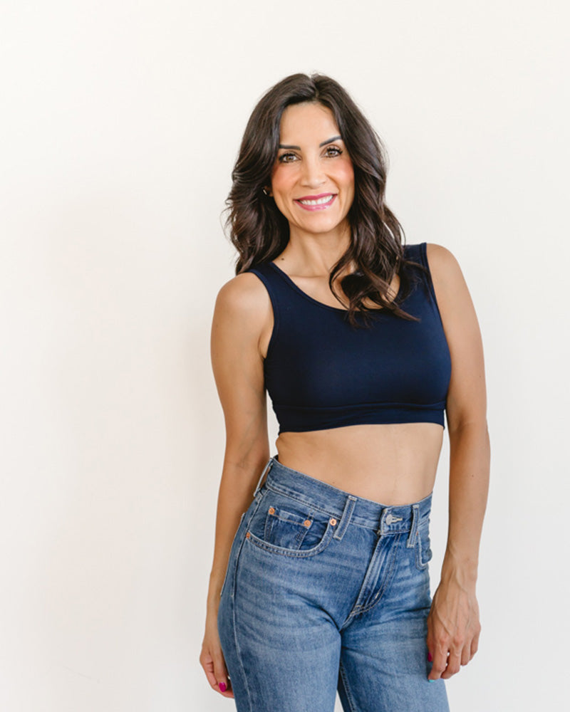 Woman wearing a navy blue sports bra and blue jeans against a white background