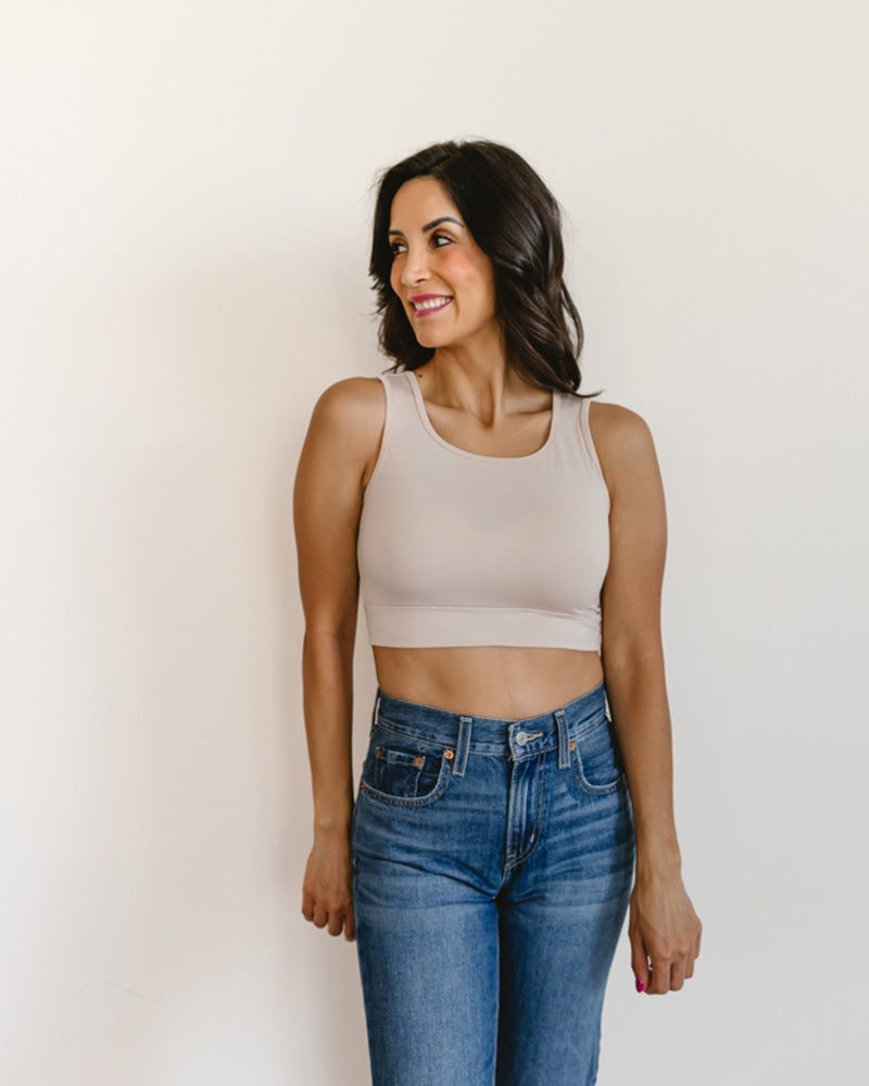 Woman wearing a beige tank top and blue jeans against a plain background
