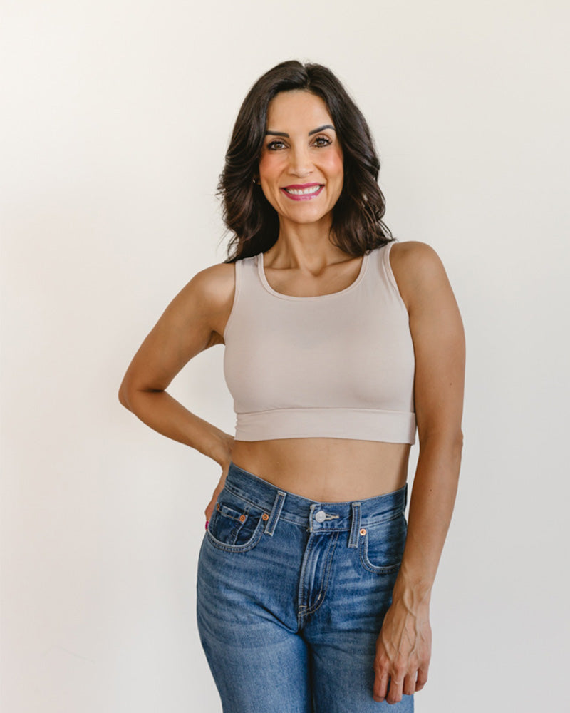 Woman wearing a beige sports bra and blue jeans against a plain background