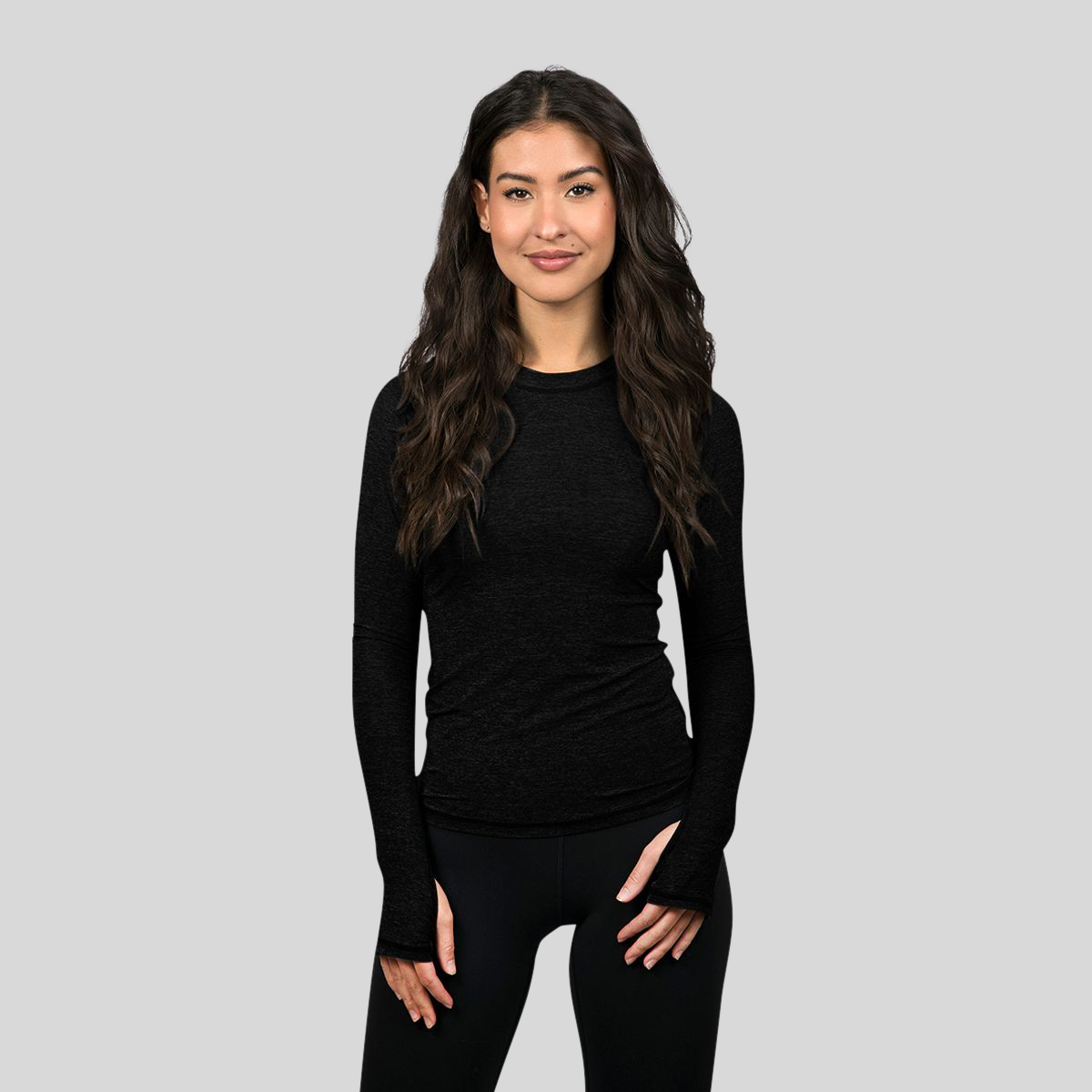 Woman wearing a black long-sleeve top and black leggings on a gray background