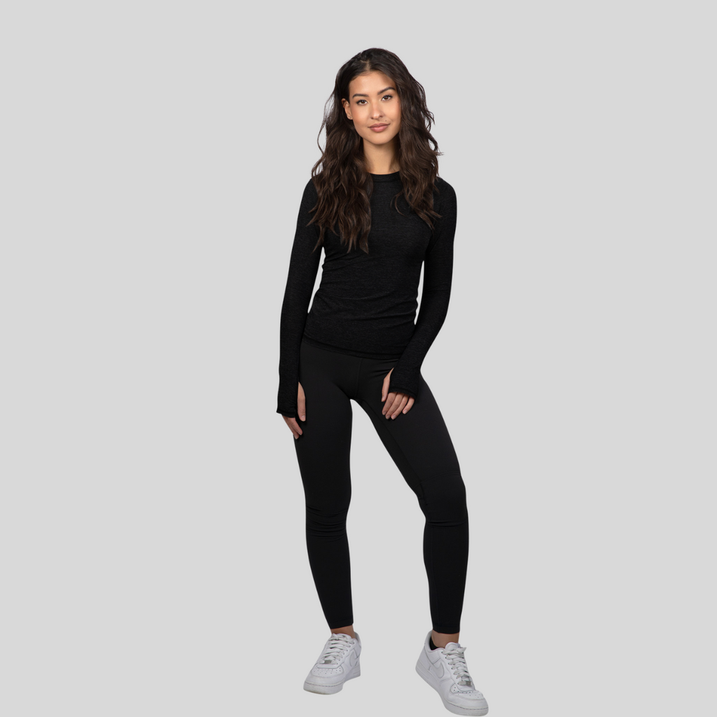 Woman wearing a black long-sleeve top and leggings on a gray background