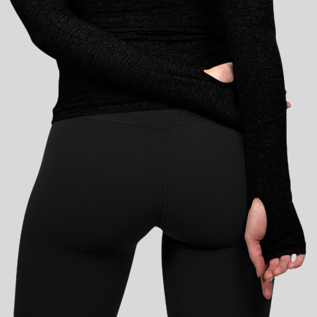 Person wearing a black long-sleeve top and black leggings on a gray background
