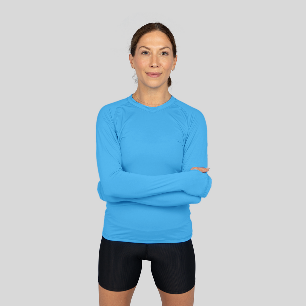 Woman wearing a blue long-sleeve athletic shirt and black shorts on a gray background