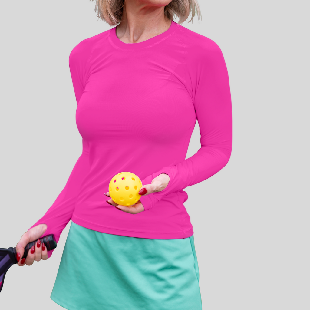 Person wearing a pink long-sleeve top and green skirt holding a yellow pickleball and paddle.