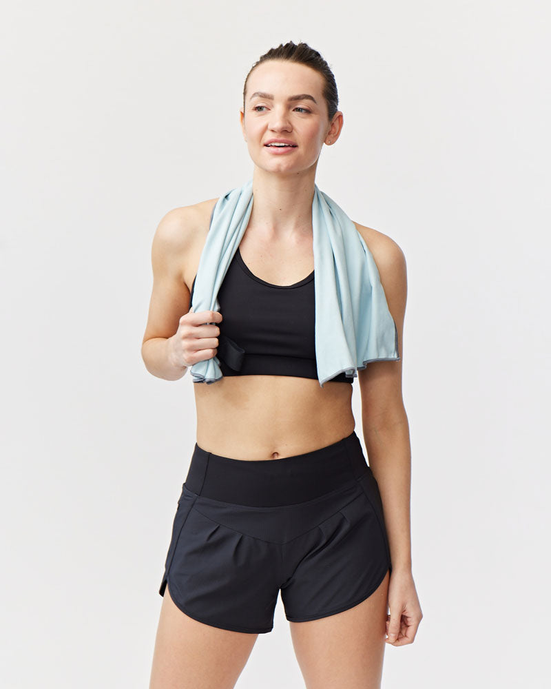 Woman in athletic wear with a towel draped over her shoulders against a light gray background