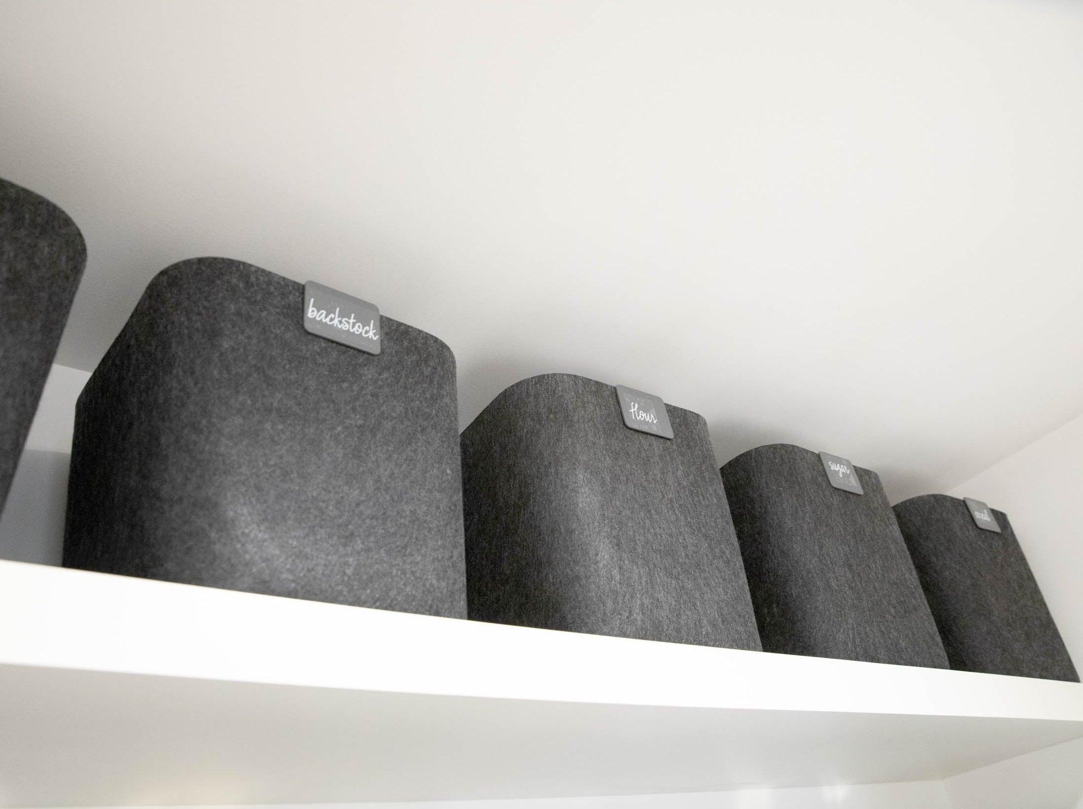 Row of gray cylindrical objects with 'Backstack' labels on a white shelf.