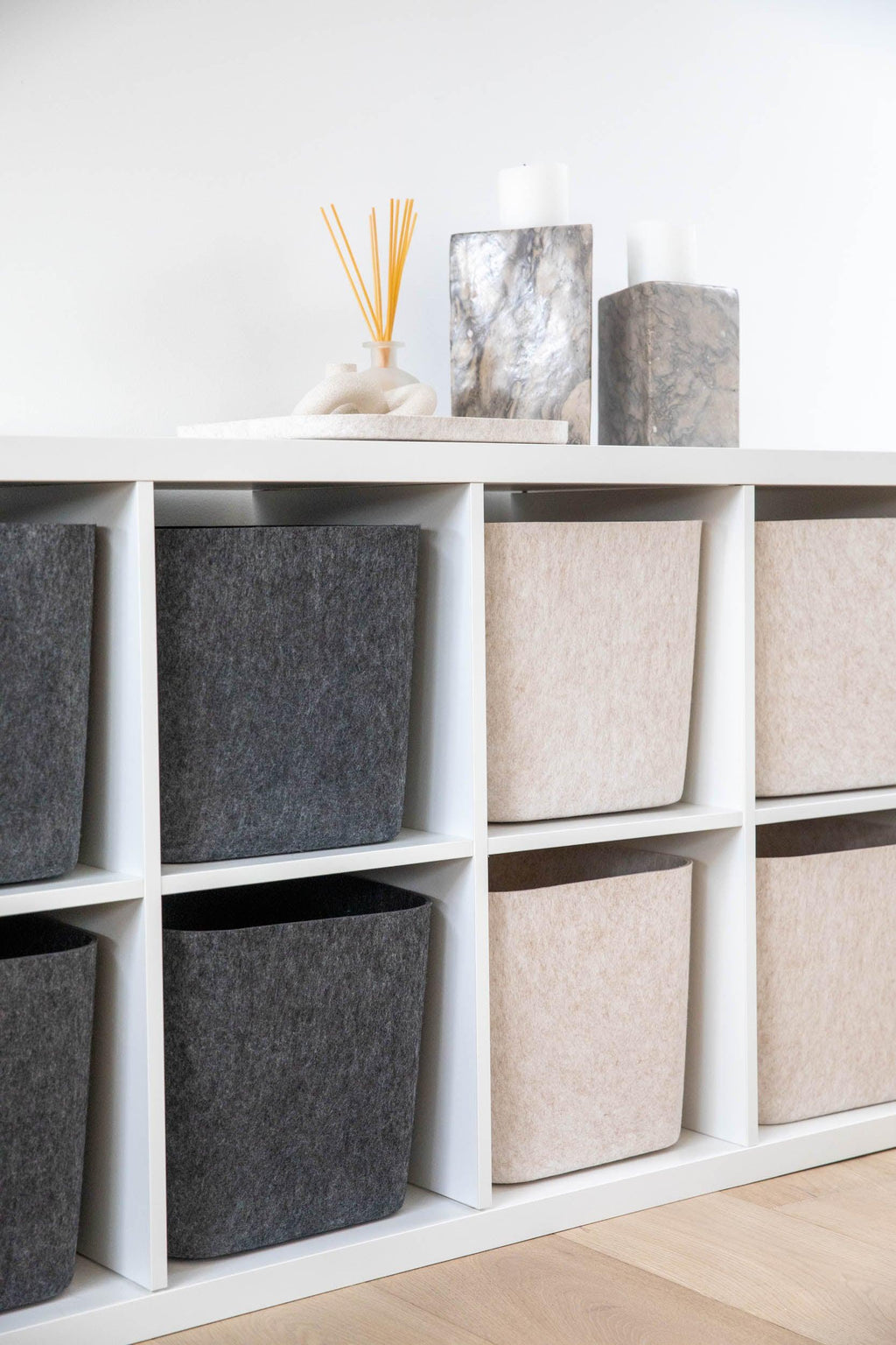 White shelving unit with gray and beige storage bins against a white wall.