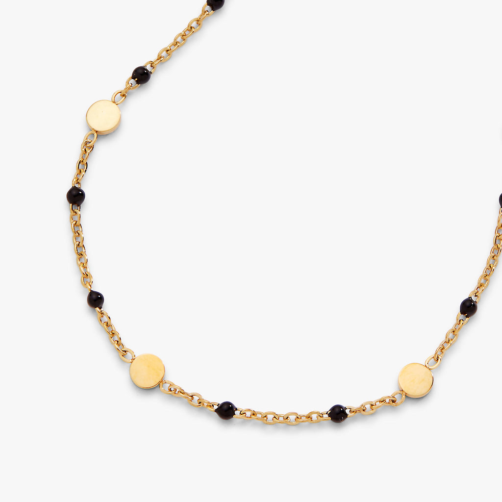 Gold necklace with black beads on a white background