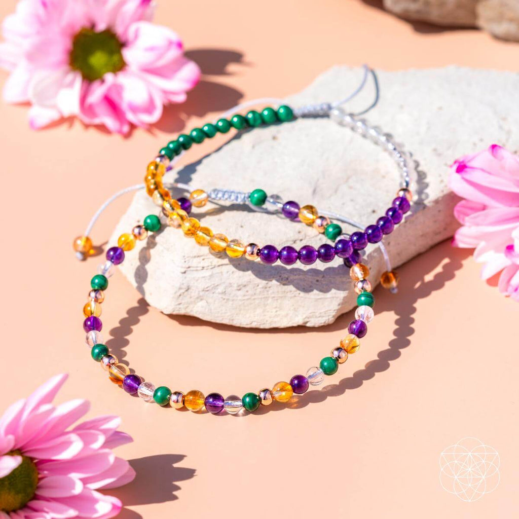 Colorful beaded bracelets on a rock with pink flowers