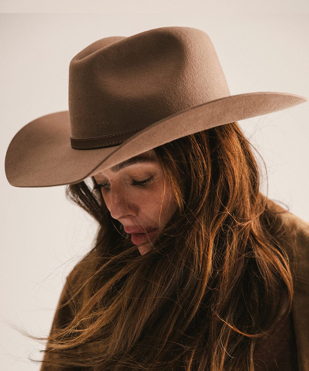Person wearing a brown cowboy hat and coat against a neutral background