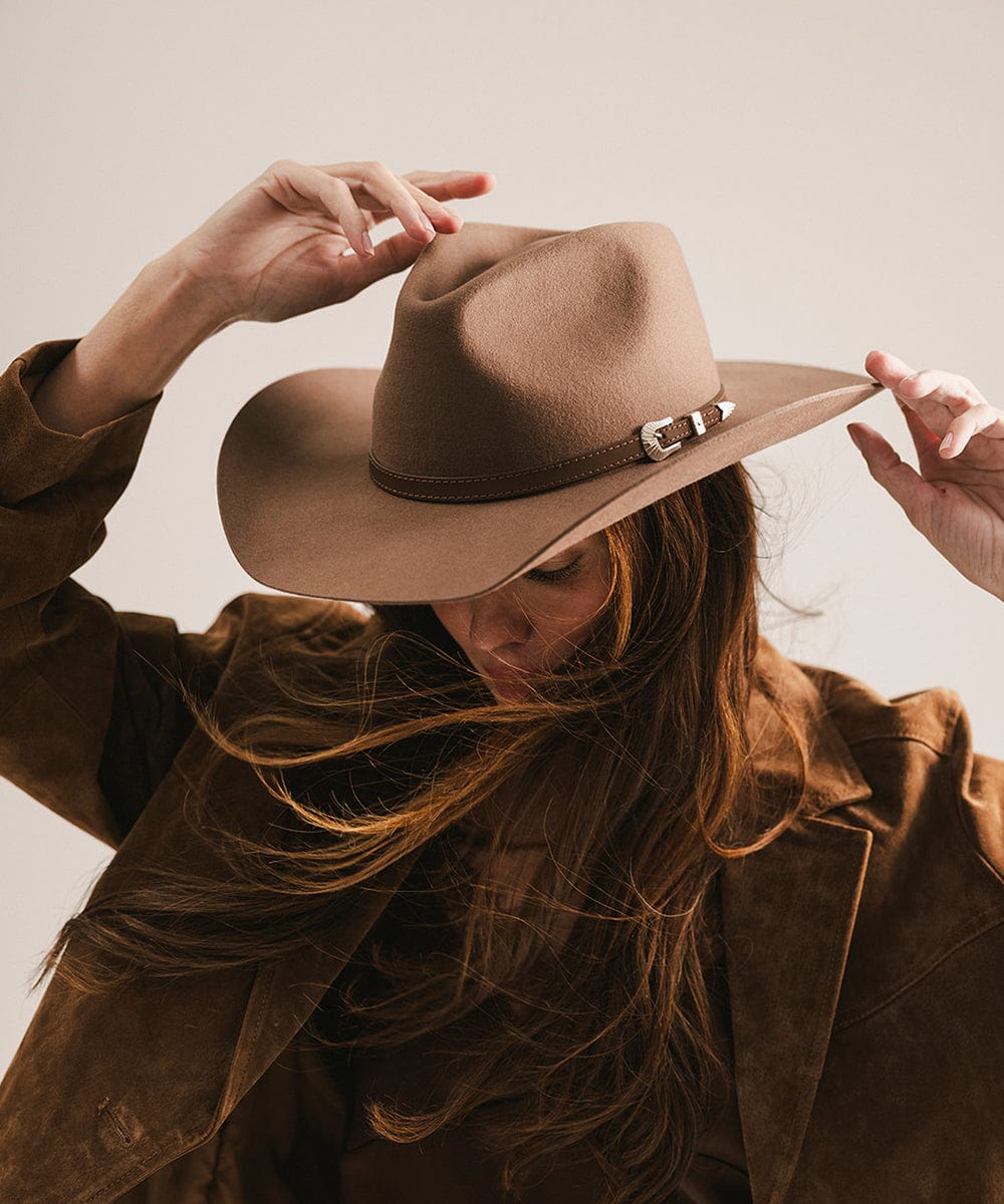 Person wearing a brown hat and coat against a neutral background