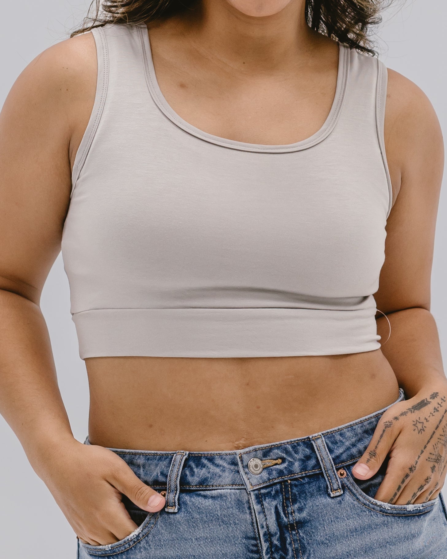 Person wearing a beige crop top and blue jeans on a plain background