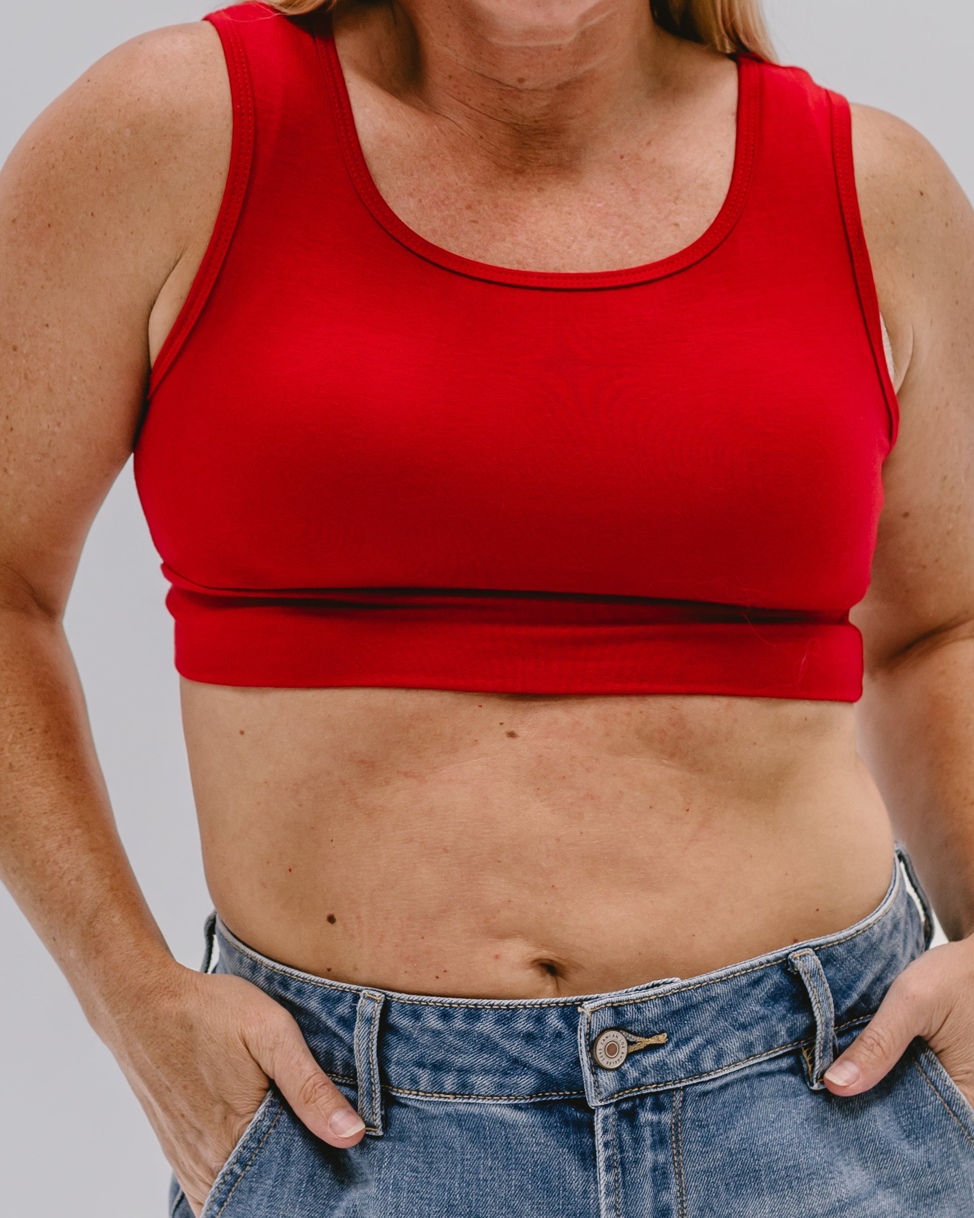 Person wearing a red tank top and blue jeans on a plain background