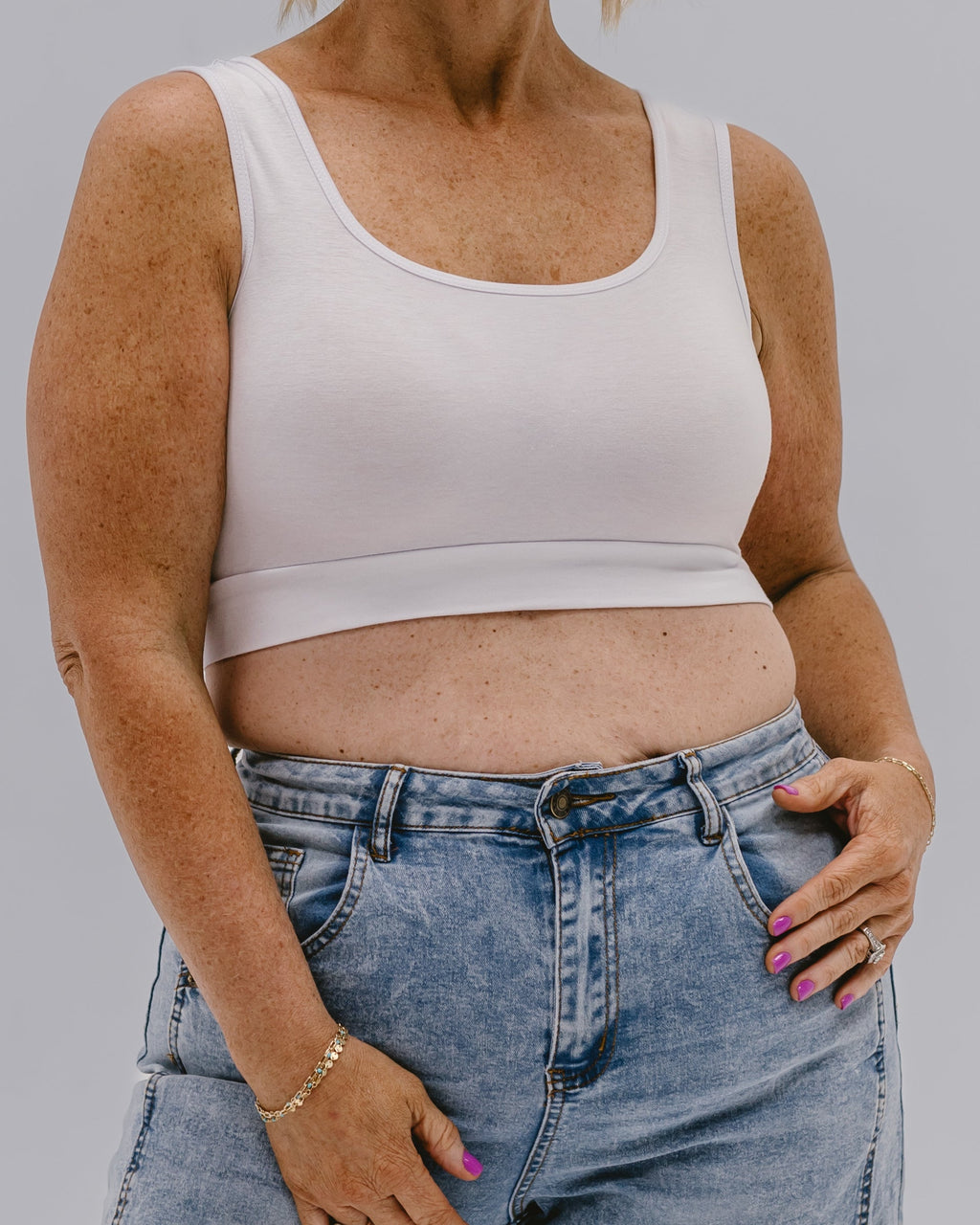 Person wearing a white tank top and blue jeans on a gray background