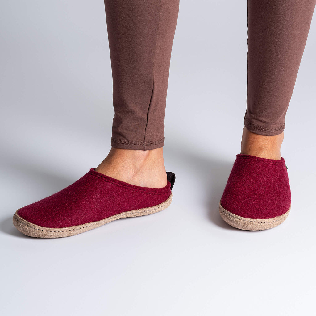 Red slippers worn with brown pants on a light gray background