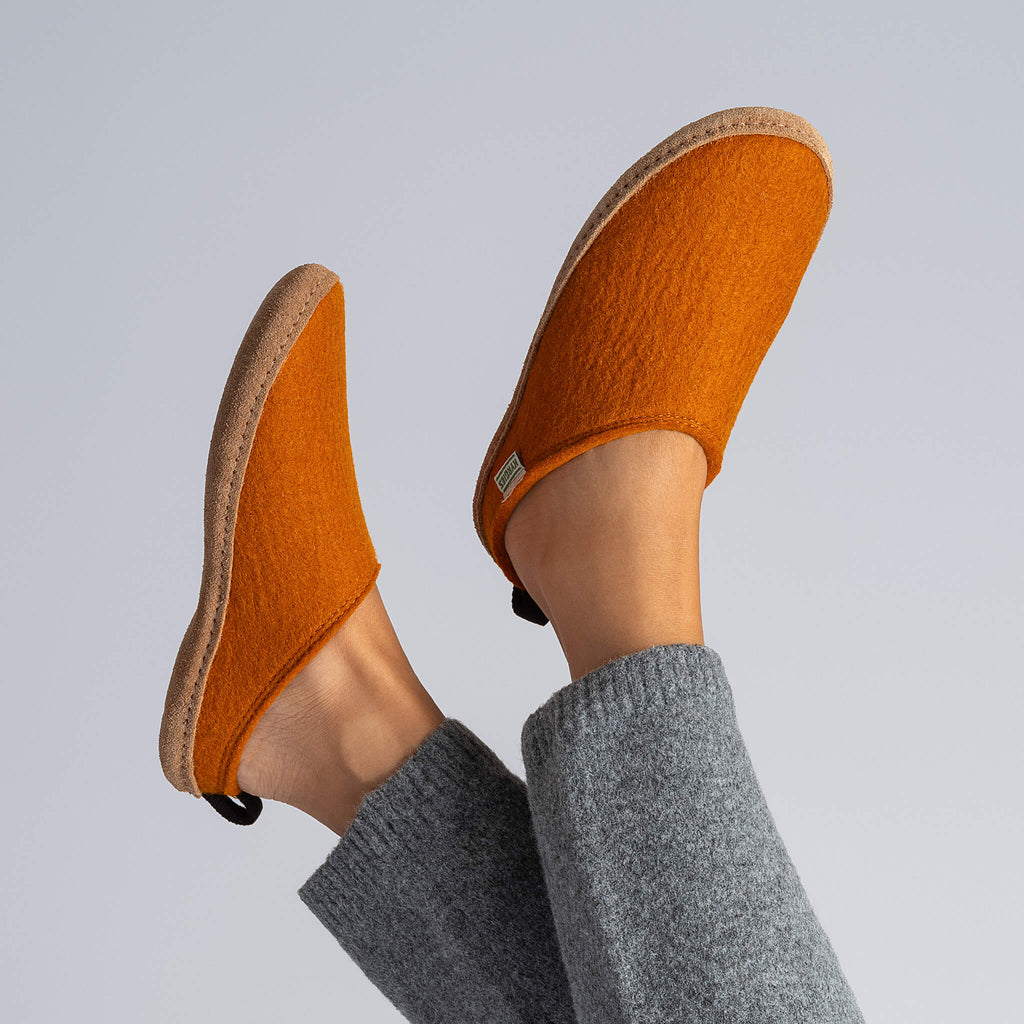 Orange slippers worn with gray pants on a light gray background