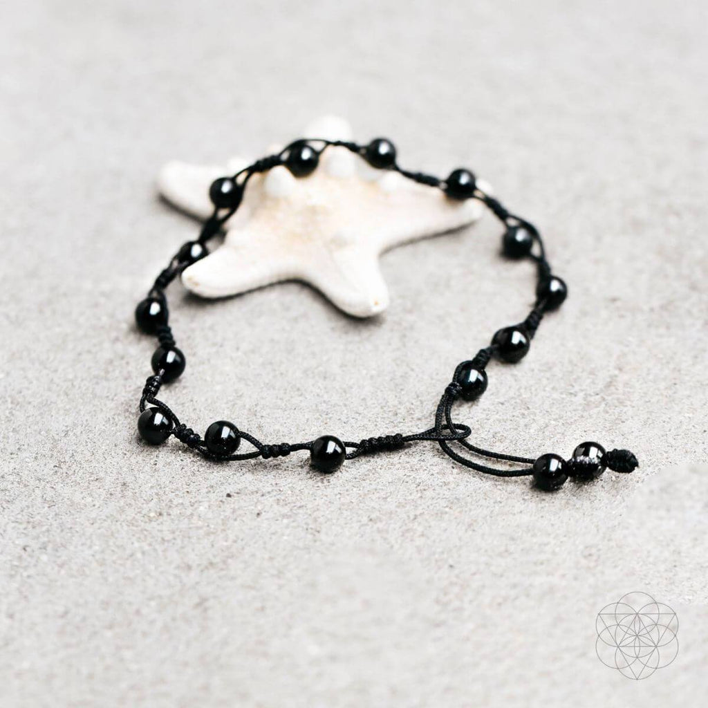 Black beaded bracelet on a sandy surface with a starfish