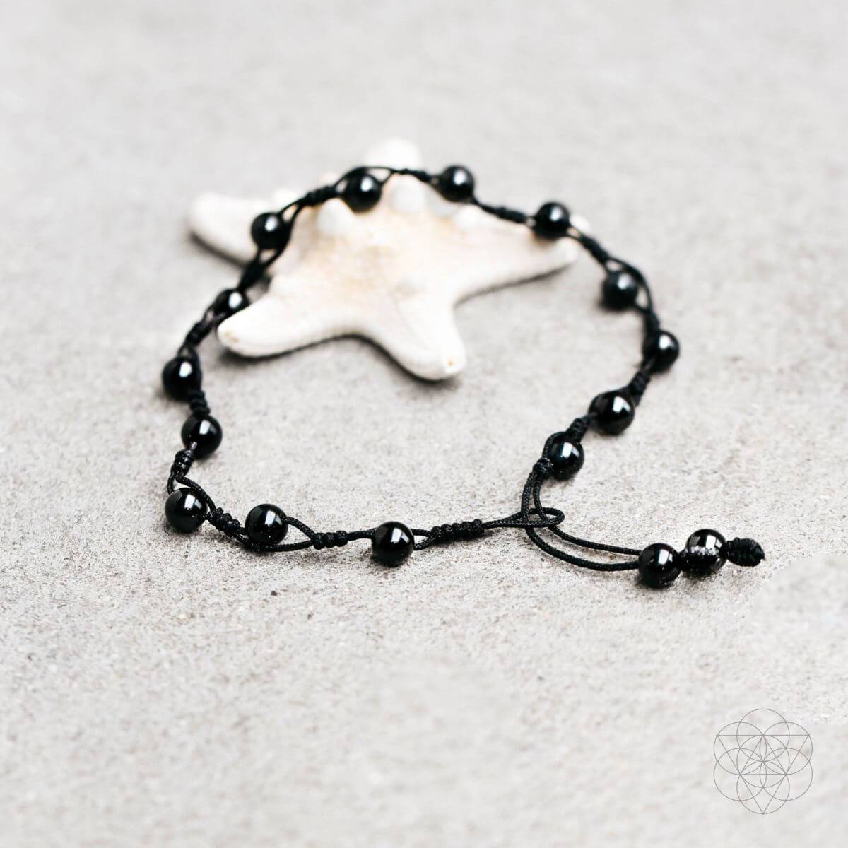 Black beaded bracelet on a sandy surface with a starfish