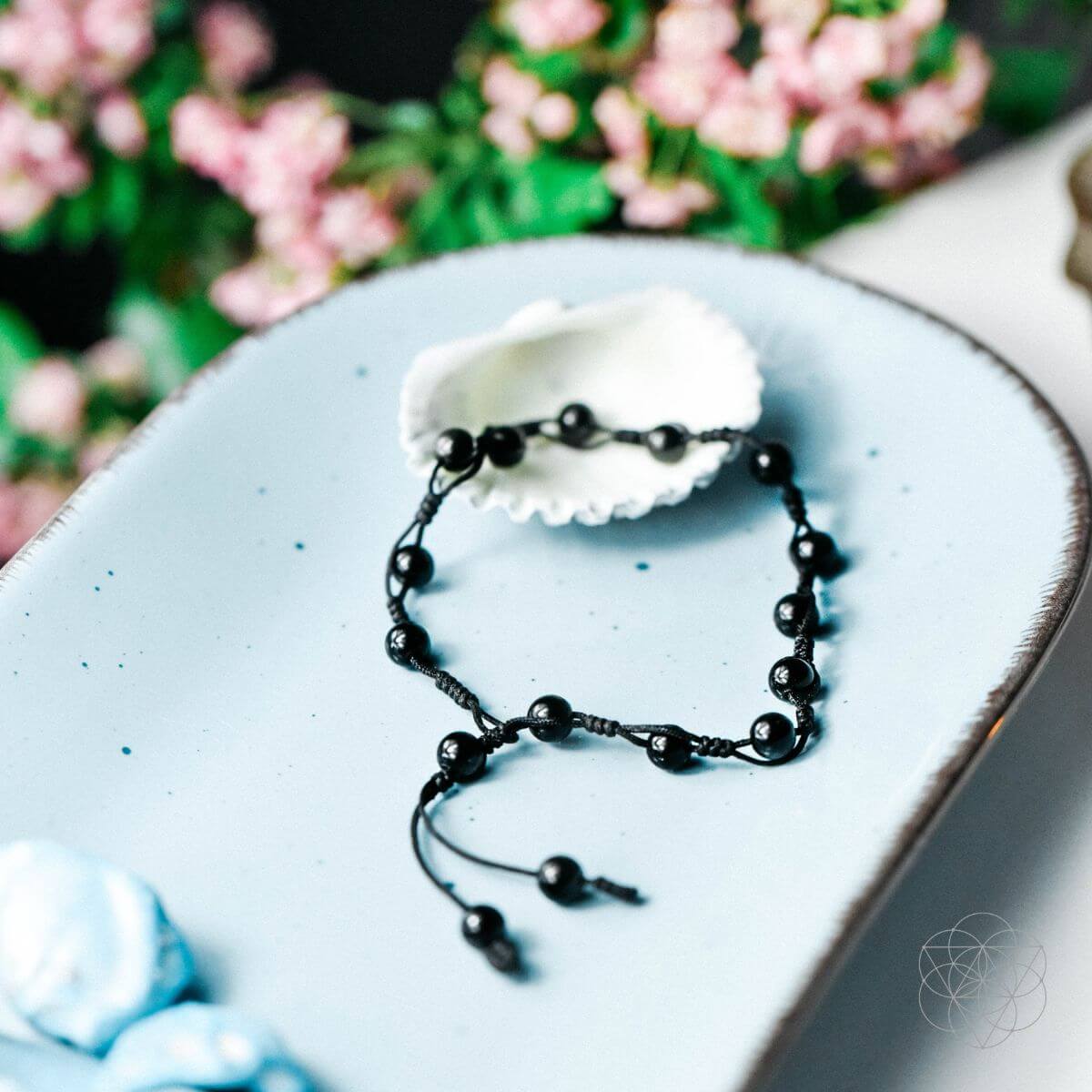 Black beaded bracelet on a light blue ceramic plate with pink flowers in the background