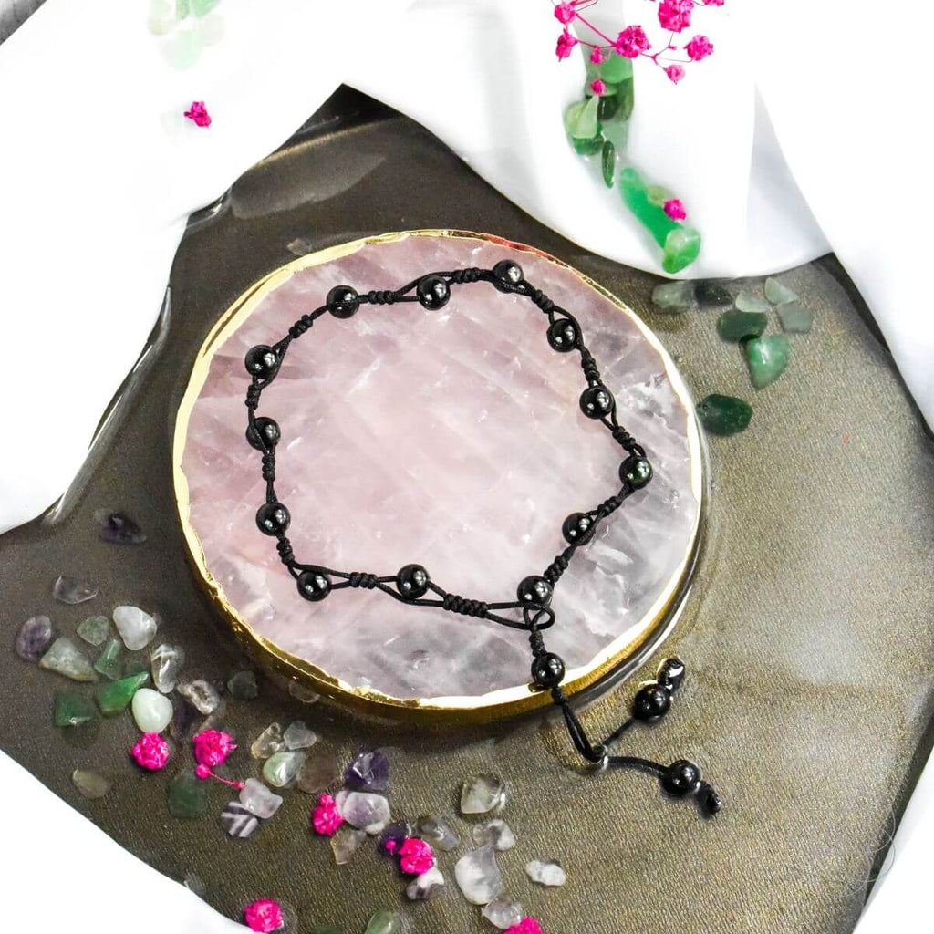 Black beaded bracelet on a pink crystal with decorative stones and flowers in the background
