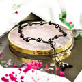 Black beaded necklace on a pink crystal with decorative background