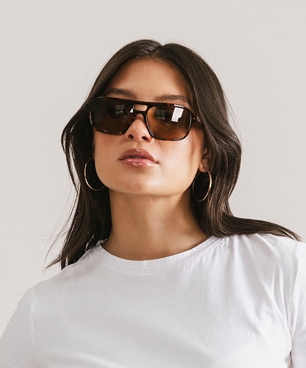 Woman wearing sunglasses and a white shirt against a plain background