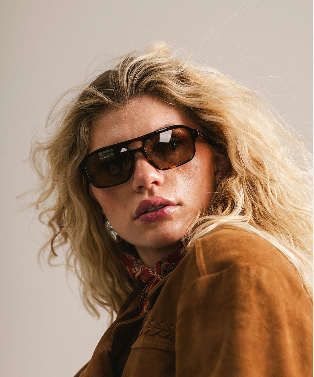 Person wearing sunglasses and a brown jacket with a neutral background
