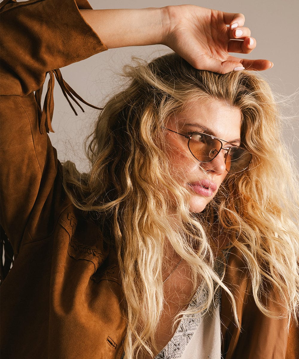 Woman with sunglasses and a brown leather jacket against a neutral background