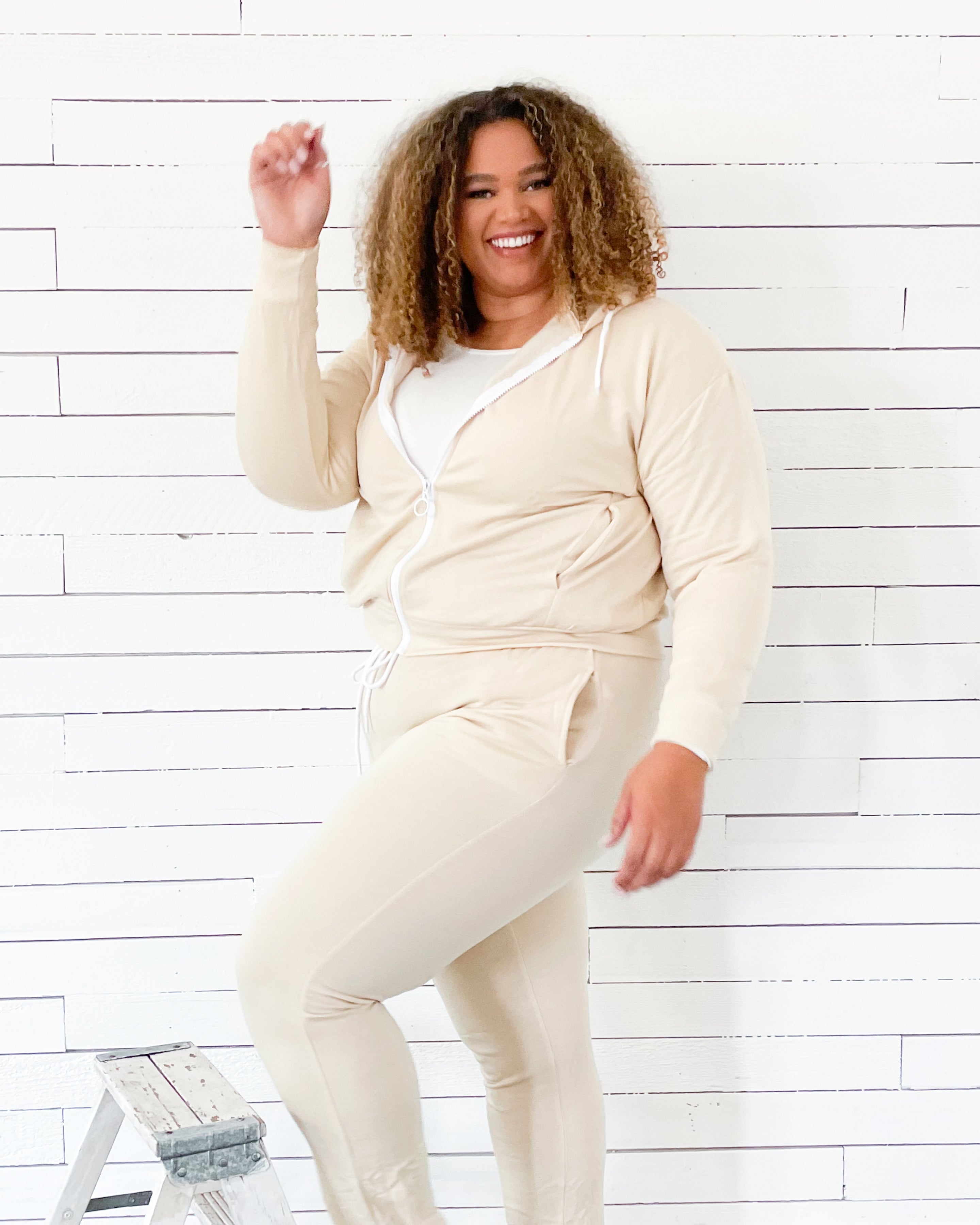 Person wearing a cream-colored outfit against a white wooden panel background