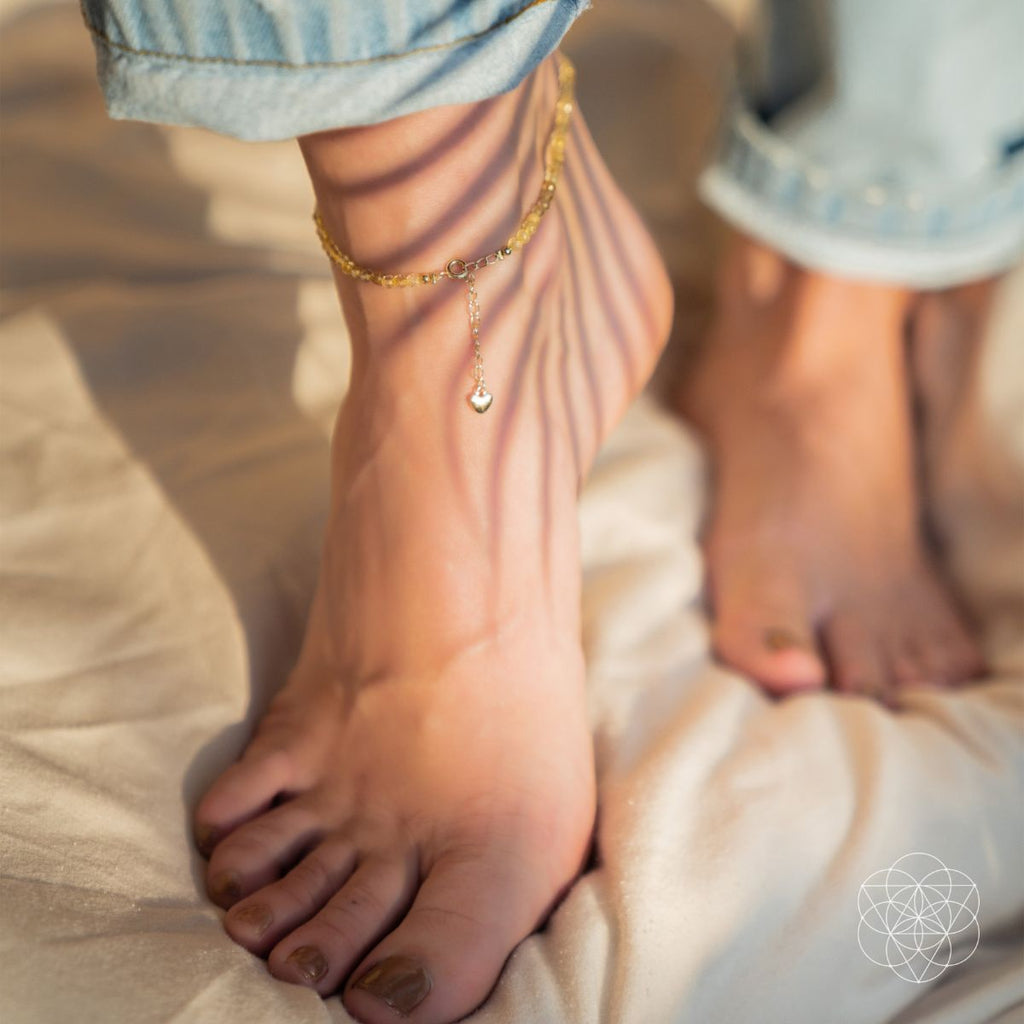 Close-up of feet wearing anklets on a soft surface