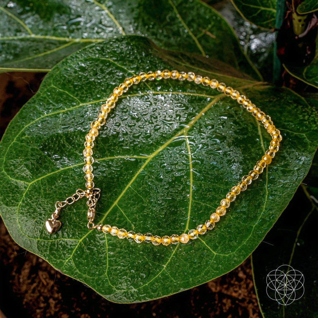 Gold beaded bracelet with a heart charm on a green leaf