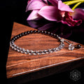 Silver bracelet on a wooden surface with pink flowers in the background