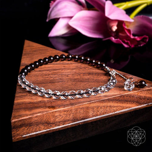 Silver bracelet on a wooden surface with pink flowers in the background