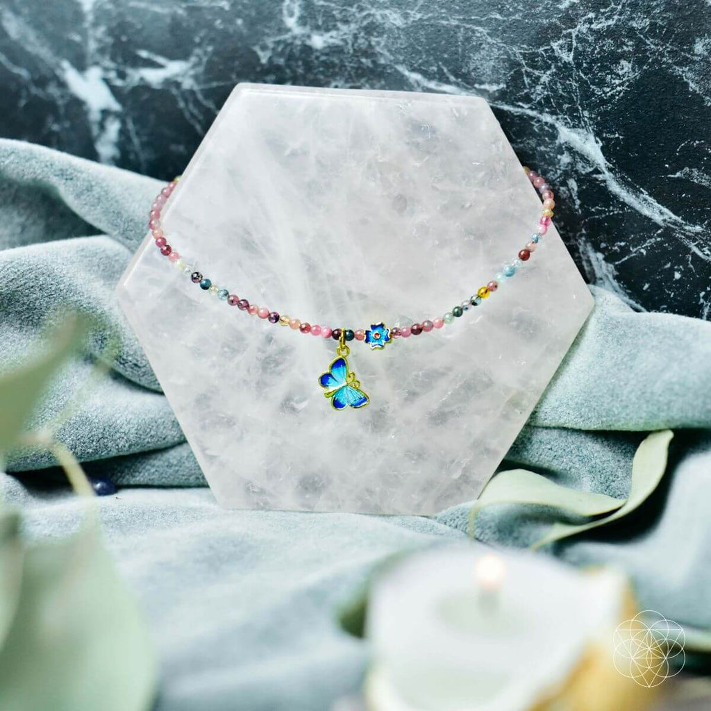 Colorful beaded bracelet with a butterfly charm on a marble stand against a marble background.