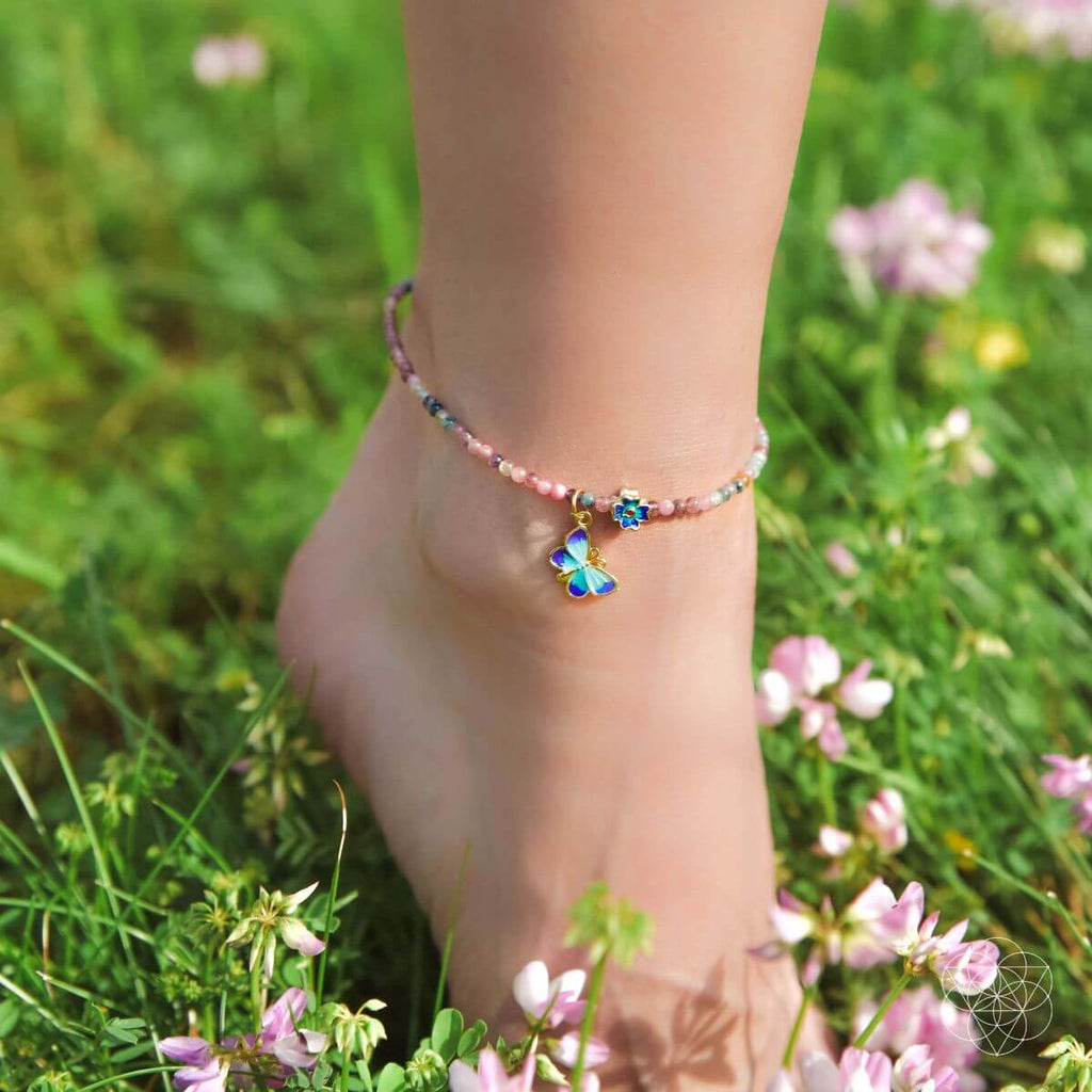 Ankle bracelet with butterfly charm on a foot in a grassy field with flowers
