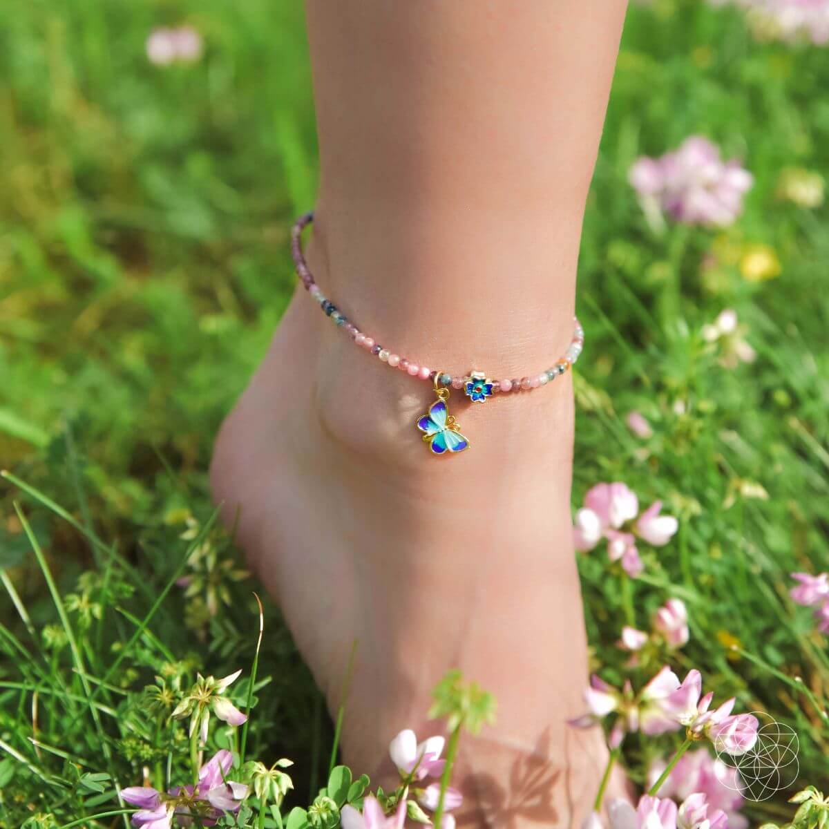 Ankle bracelet with butterfly charm on a foot in a grassy field with flowers