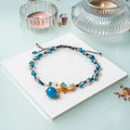 Necklace with blue and gold beads on a white square, with candles in the background