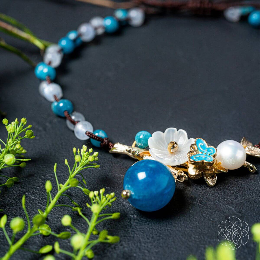 Necklace with blue and white beads and floral elements on a dark surface with green leaves.