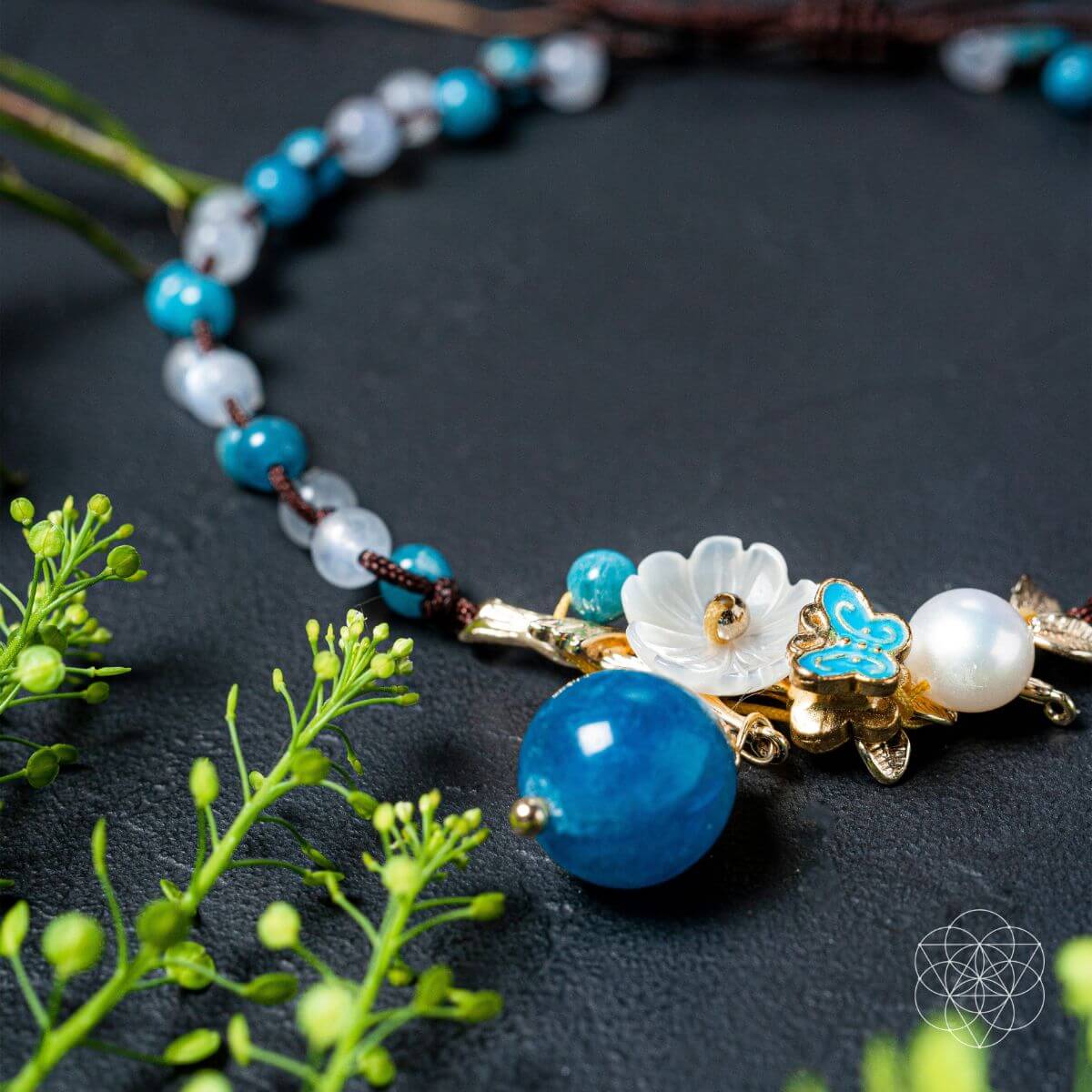 Necklace with blue and white beads and floral elements on a dark surface with green leaves.